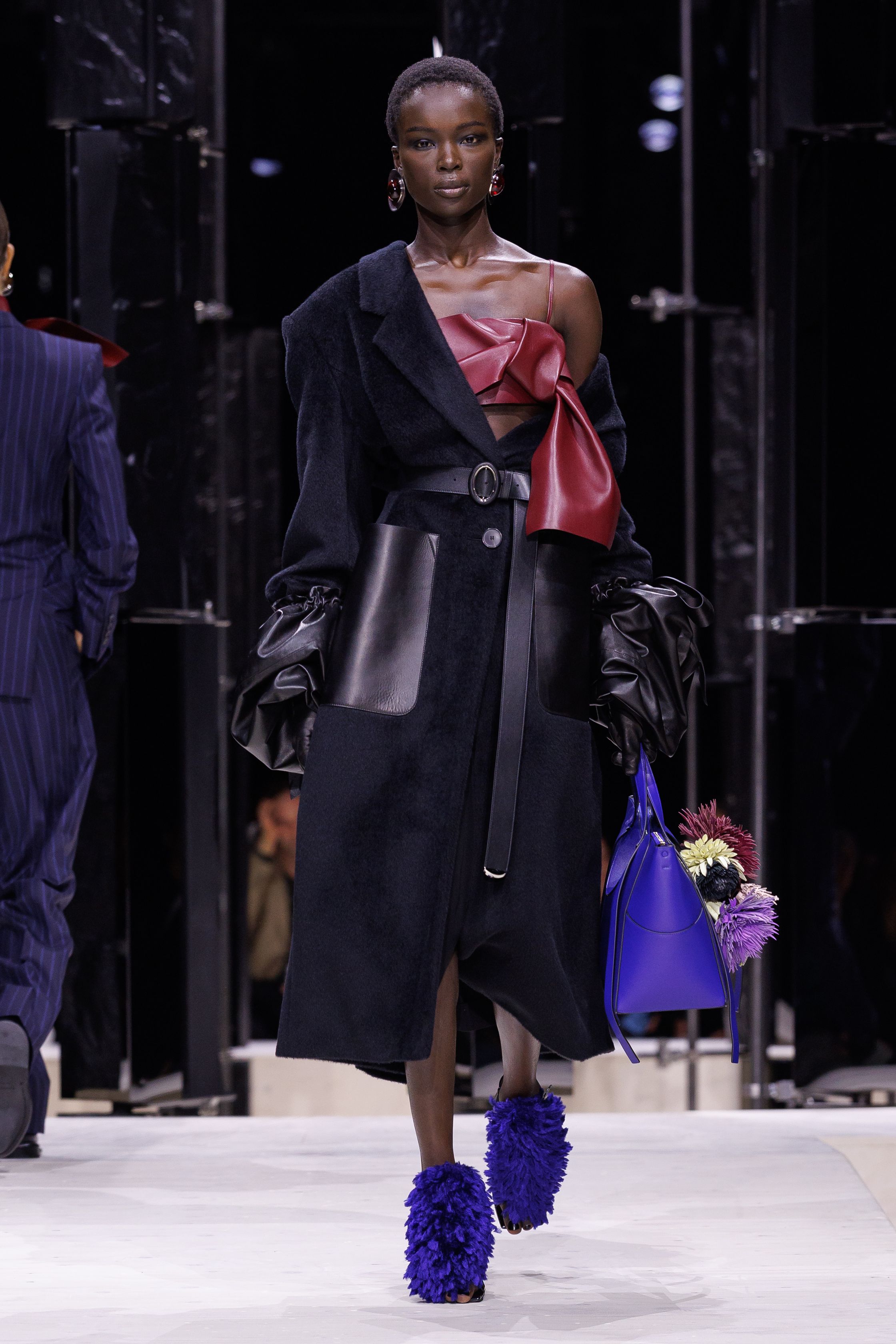 Givenchy 2026秋冬在现代建筑空间中呈现一场充满戏剧性的时装叙事：雕塑式西装、亮色斗篷、结构礼服与夸张装饰共同构建品牌标志性的高级时装气质。蓝色、红色与黄色的高饱和色彩与黑白经典形成鲜明对比，服装通过立体剪裁与夸张廓形展现出强烈视觉张力。整场系列在优雅与戏剧之间取得平衡，展现现代高级时装的力量-顽石频道趋势研究